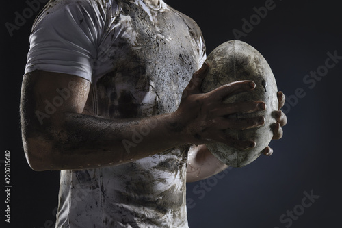 Rugby player hands with ball on dark background. Close up photo