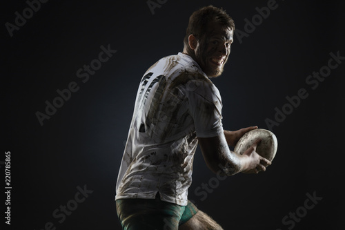 Isolated dirty rugby player with rugby ball on dark background