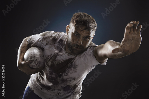 Isolated dirty rugby player with rugby ball on dark background