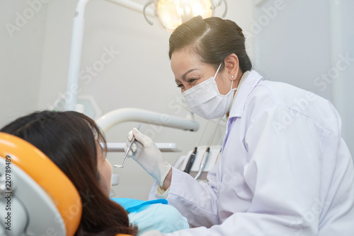 Professional adult Asian woman in mask and gloves working with anonymous woman in dental chair
