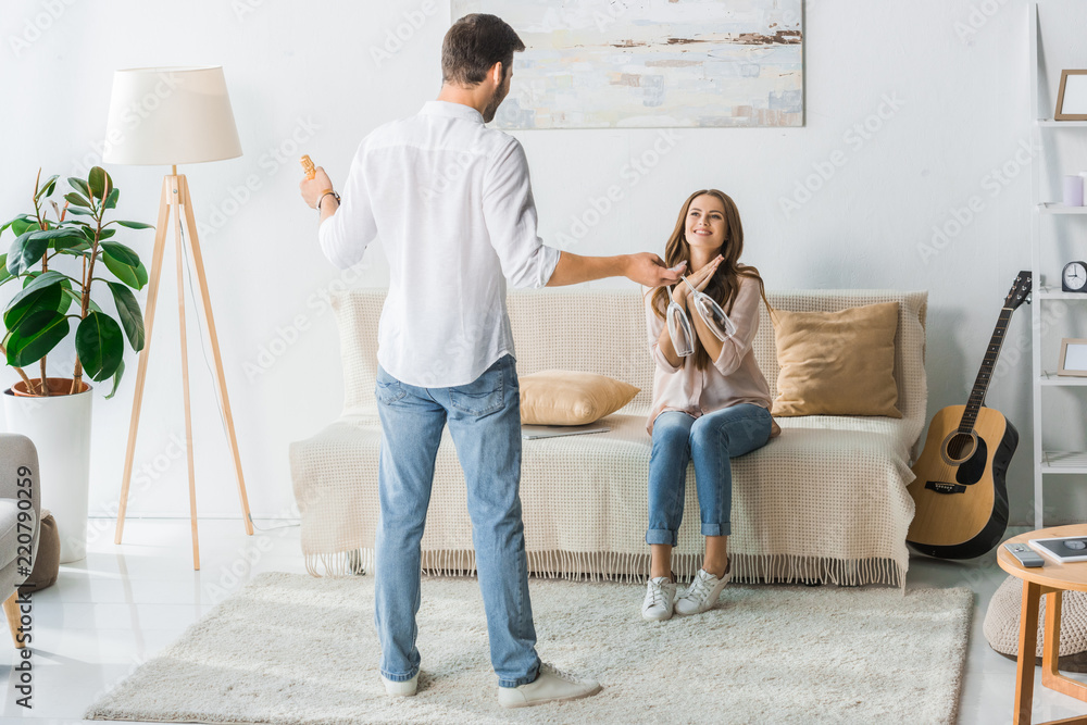 rear view of man standing with glasses and bottle of champagne while his girlfriend sitting on couch at home rear view of man standing with glasses and bottle of champagne while his girlfriend sitting on couch at home