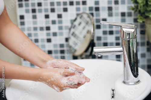 Crop side view of woman washing hands with soapy foam in white sink in bathroom