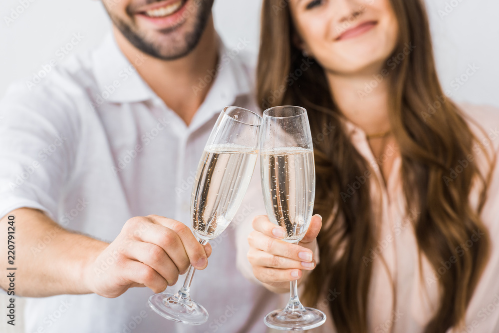 partial view of smiling couple clinking glasses of champagne on sofa at new home