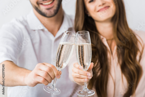 partial view of smiling couple clinking glasses of champagne on sofa at new home