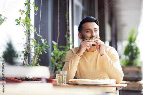 Young man enjoying taste of original Italian pizza while sitting in modern cafe