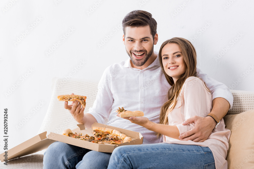 portrait of smiling young couple with pizza on sofa at home