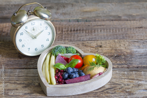 Time on diet concept with alarm clock and healthy food in heart