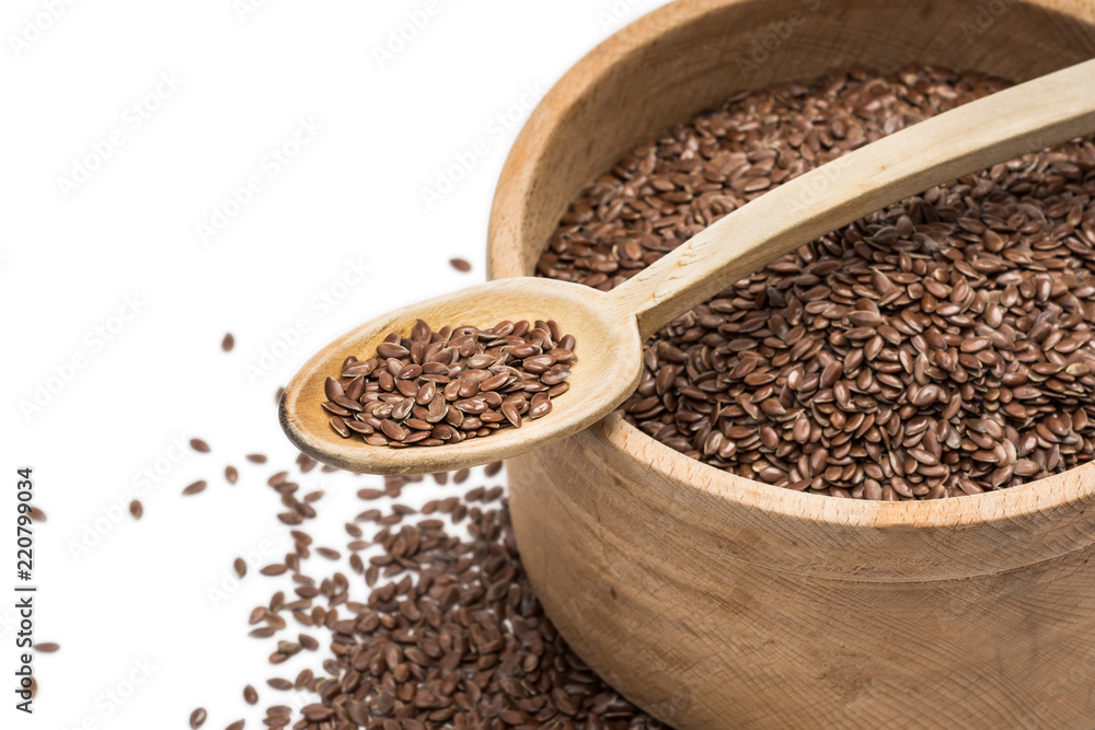 Close up of linseeds or flax seeds in wooden spoon on top of a wooden bowl with some spread on the blurred white background seen obliquely from above Close up of linseeds or flax seeds in wooden spoon on top of a wooden bowl with some spread on the blurred white background seen obliquely from above