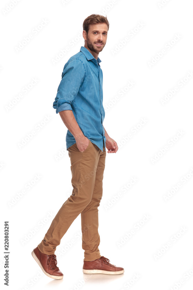 Fototapeta premium smiling young casual man moving forward with hand in pocket