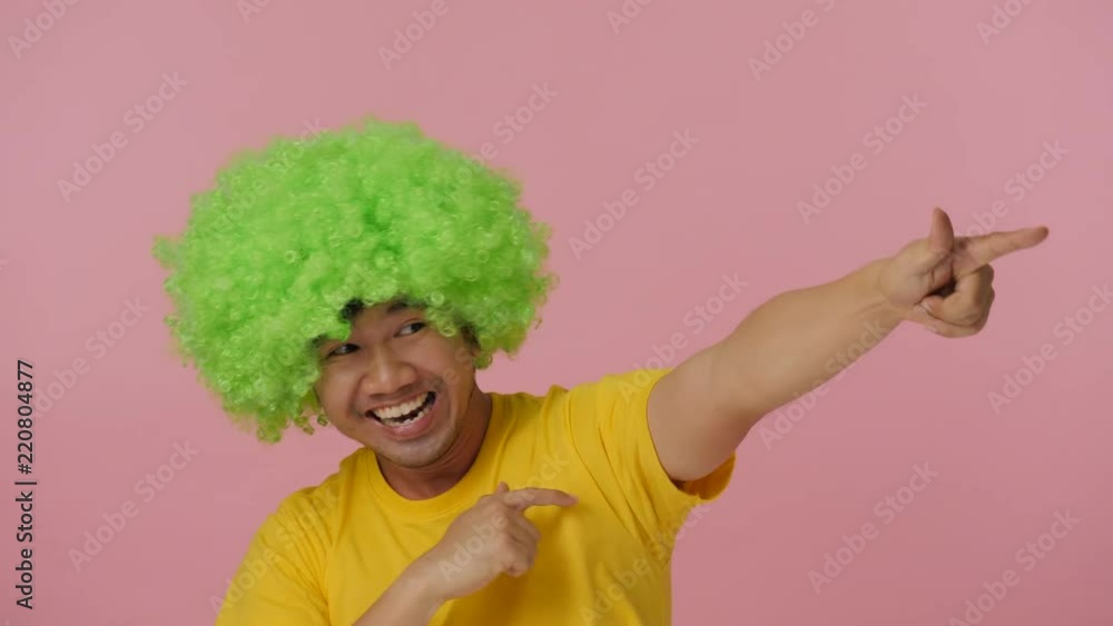 Young crazy man with colored afro wig expressing happiness on pink background. Young crazy man with colored afro wig expressing happiness on pink background.