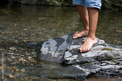 LEGS OF A CHILD PLAYING IN THE RIVER SHORE ON SUMMER