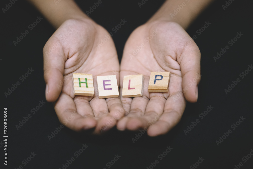 wooden alphabet tiles word HELP in a child hand over dark background. concept of help, charity and donation