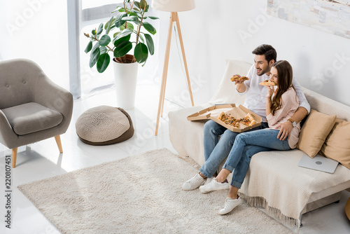 high angle view of young couple eating pizza while watching tv at home