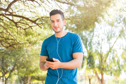 Man Using Mobile Phone And Earphones Before Workout In Park