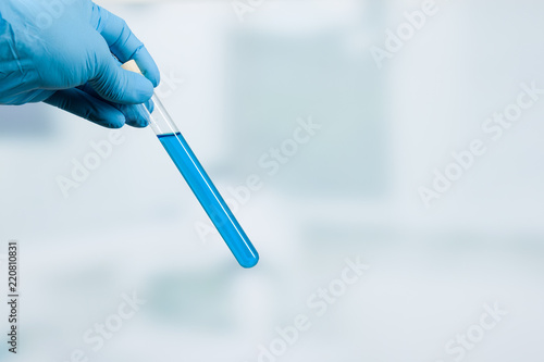Hand eines Wissenschaftlers hält Reagenzgläser mit blauer Flüssigkeit vor Labor im Hintergrund