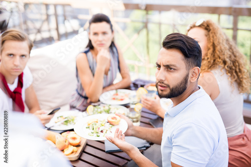 Photography Portrait of frowning Middle-Eastern man complaining about food during lunch with