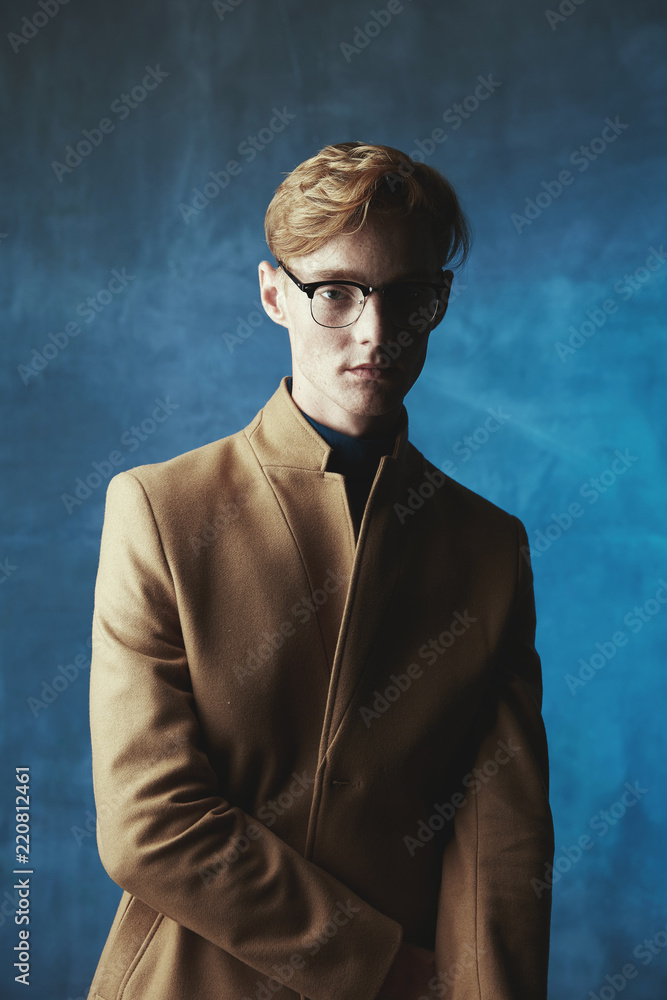 Dark studio portrait of young male model with red hair and freckles. Weared  in brown coat and glasses. Blue light and background. Stock Photo | Adobe  Stock