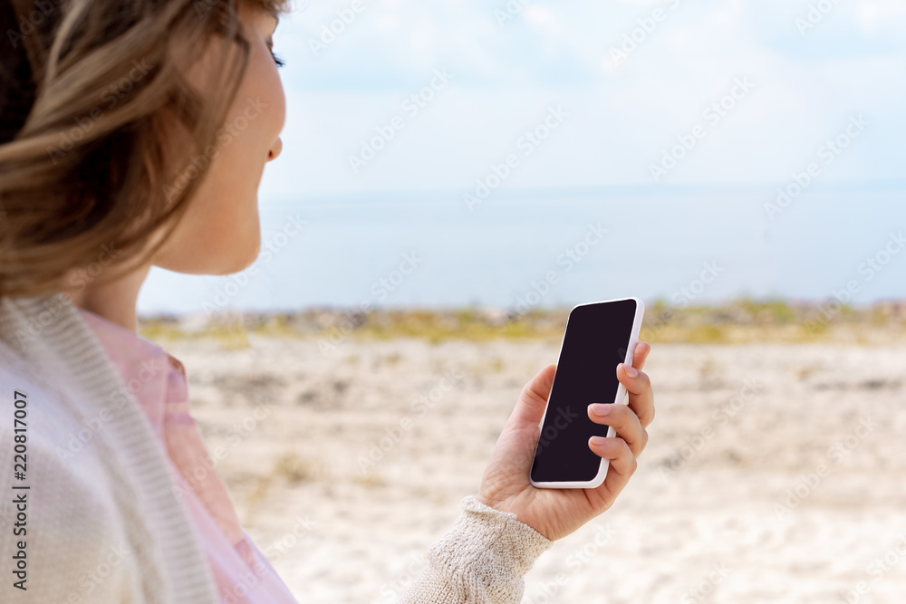 partial view of woman using smartphone with blank screen on sandy beach