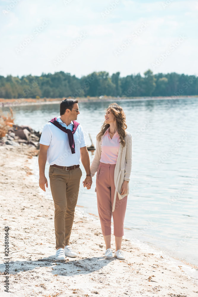 romantic couple holding hands while walking on sandy riverside romantic couple holding hands while walking on sandy riverside