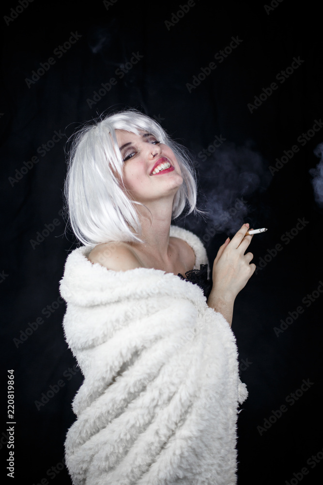 Attractive young woman in costume smoking cigar and looking at camera while standing on black background Attractive young woman in costume smoking cigar and looking at camera while standing on black background