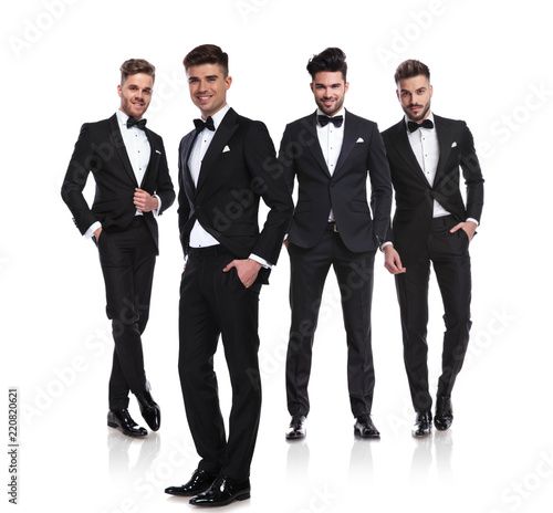 Obraz na plátně four elegant men in tuxedoes standing with hands in pockets