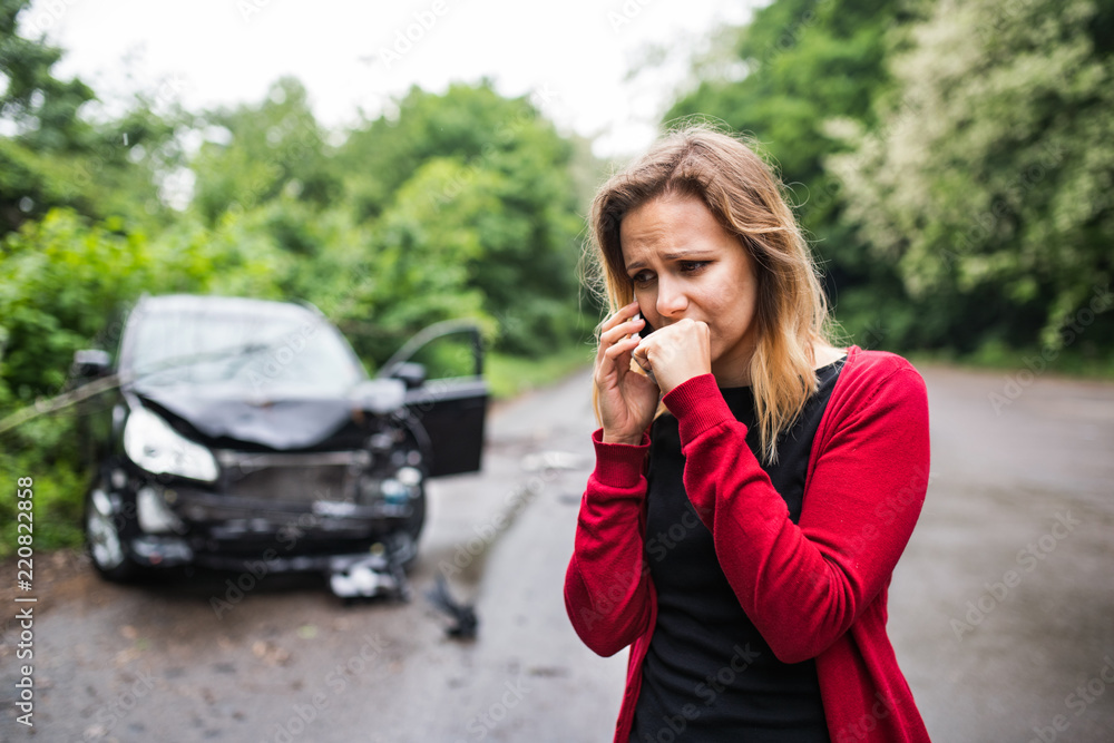 A young woman with smartphone by the damaged car after a car accident, making a phone call. A young woman with smartphone by the damaged car after a car accident, making a phone call.
