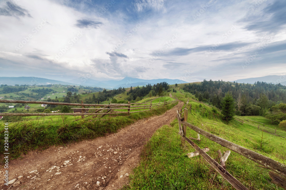 old wooden fence, rural road and  top of mountain on horizon on sunset. summer (autumn) landscape
