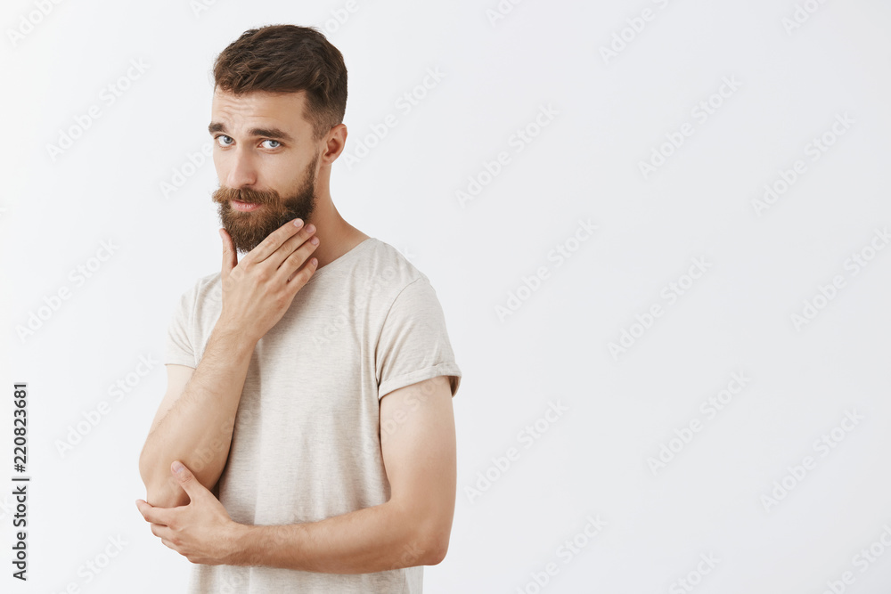 My beard is amazing. Portrait of cool and stylish unshaven male model with trendy hairstyle rubbing bristle standing half-turned with sensual and self-assured expression posing over gray background My beard is amazing. Portrait of cool and stylish unshaven male model with trendy hairstyle rubbing bristle standing half-turned with sensual and self-assured expression posing over gray background