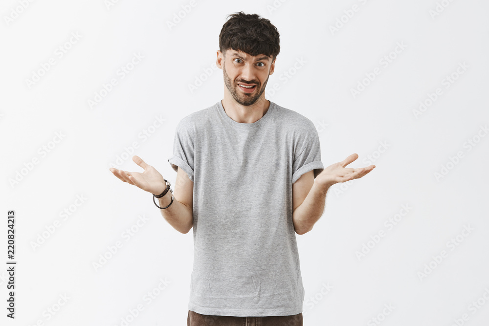 Studio shot of man explaining something simple being questioned someone cannot understand shrugging with spread palms frowning and grimacing with clueless expression over gray wall Studio shot of man explaining something simple being questioned someone cannot understand shrugging with spread palms frowning and grimacing with clueless expression over gray wall