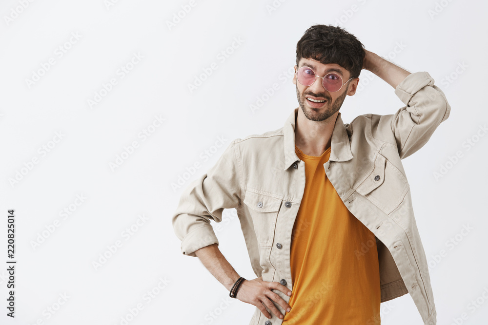 Indoor shot of stylish adult caucasian man in trendy sunglasses yellow t-shirt and shirt scratching head and looking confused and uncertain at camera having doubts over gray background Indoor shot of stylish adult caucasian man in trendy sunglasses yellow t-shirt and shirt scratching head and looking confused and uncertain at camera having doubts over gray background