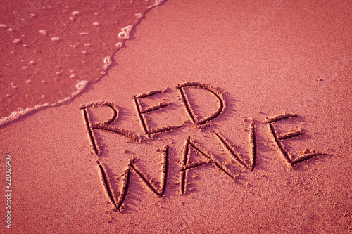 'RED WAVE' written in the sand on the beach with the sea washing up the shore.