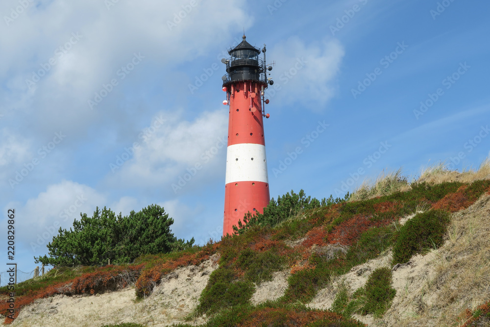Red white striped lighthouse at seaside on sunny day | Huge lighthouse located in overgrown sand dunes | Sylt, Germany 