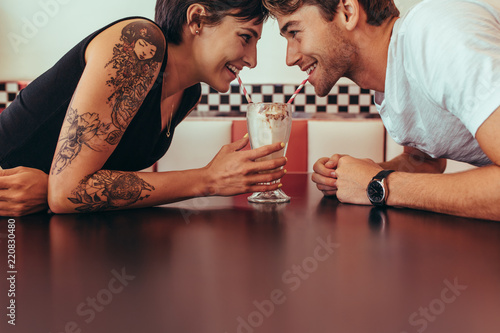 Man and woman sharing milk shake from one glass using straws