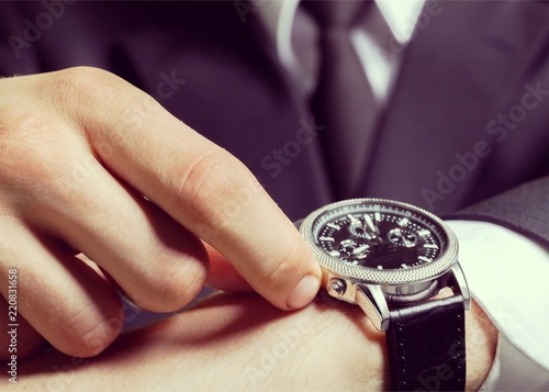 Businessman pointing at hand watch on grey wall background