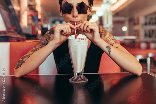 Fényképezés Woman drinking milkshake with a straw sitting at a diner