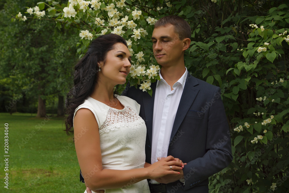 Fototapeta premium Beautiful brunette in white dress smiles next to her fiance
