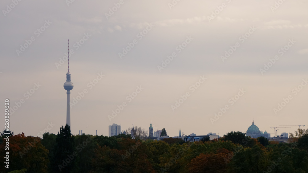 View over Berlin skyline including the Fernsehturm TV tower, with dusky overcast sky and autumnal trees