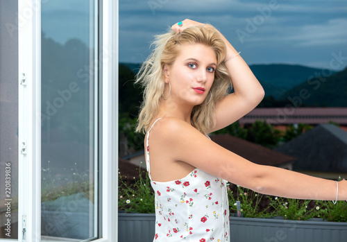 beautiful young blonde woman standing near the window