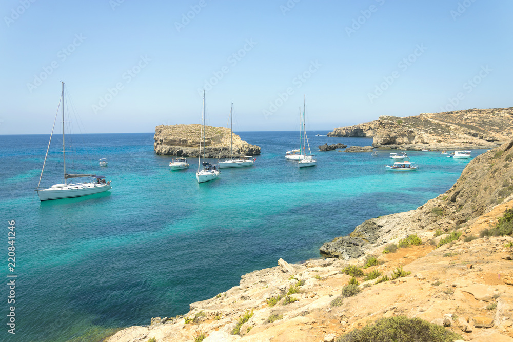 Panorama view on sail boats anchored on open sea in popular bay Blue lagoon on Comino island Malta. Turquoise sea crystal clear and azure ocean, yachts and boats, blue sky without clouds.
