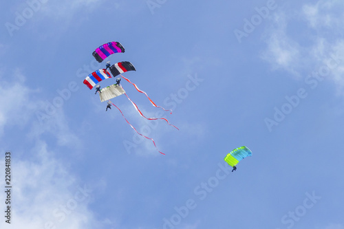 Four parachutists with colorful parachutes, Poland national flag colors wawing behind on airshow. Artists team work, cooperation. Parachuters paragliding sky performance.