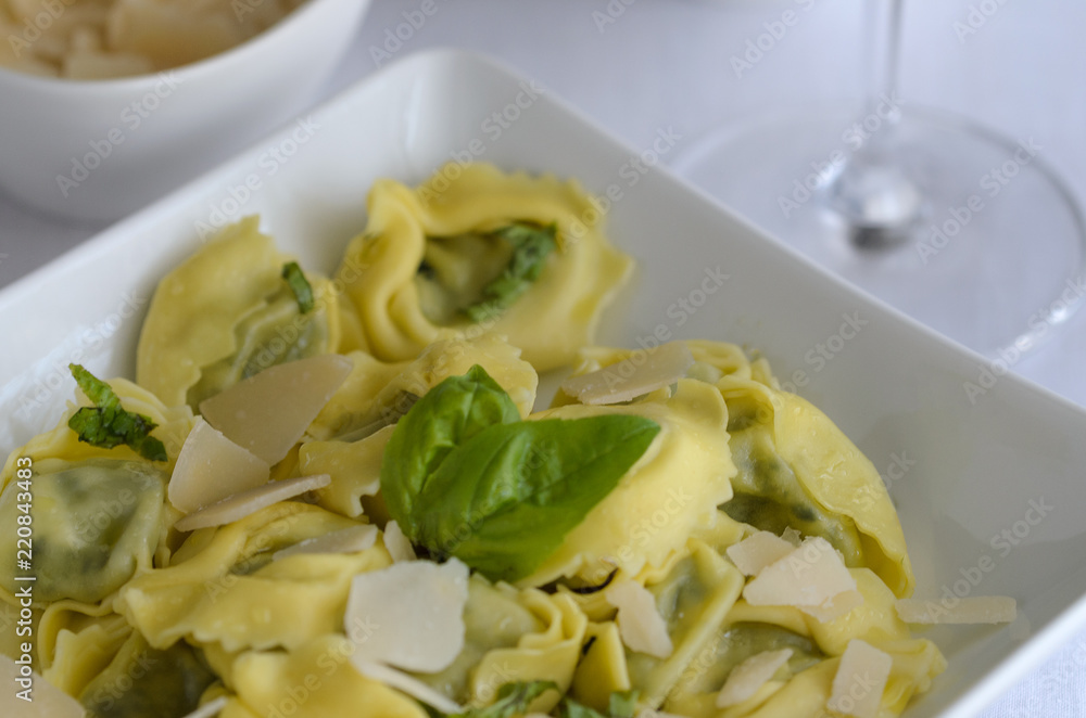 Italian ravioli filled with ricotta cheese and spinach decorated with basil, served with parmesan and pesto. Restaurant pasta dish background. Italian ravioli filled with ricotta cheese and spinach decorated with basil, served with parmesan and pesto. Restaurant pasta dish background.