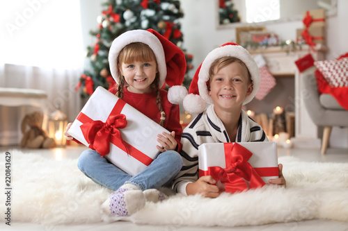 Cute little children in Santa hats with Christmas gift boxes at home