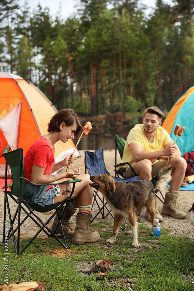 Fototapeta premium Young people having lunch with sausages near camping tents outdoors