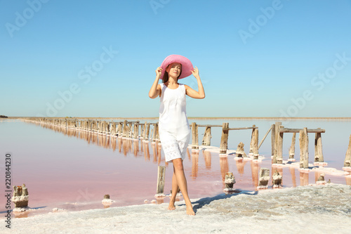 Beautiful woman with hat posing near pink lake on summer day