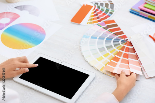 Woman with tablet and paint color palette samples at table, closeup