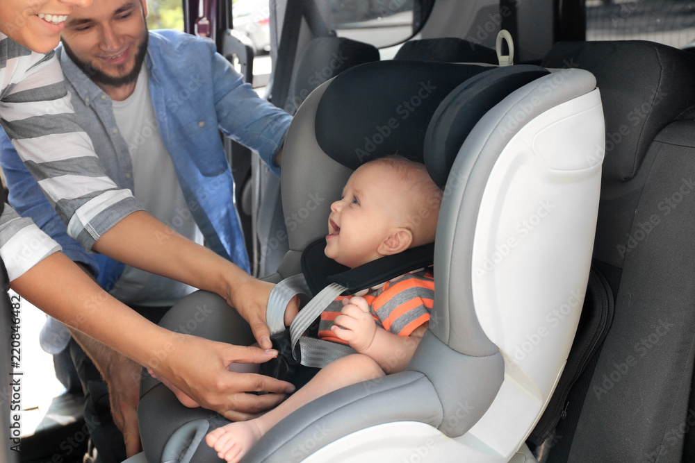 Mother fastening baby to child safety seat inside of car Mother fastening baby to child safety seat inside of car
