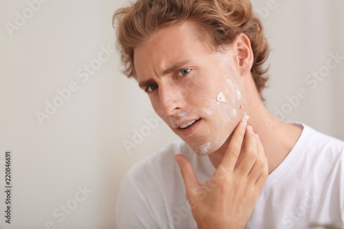 Fotografie Young man with face hurt while shaving at home