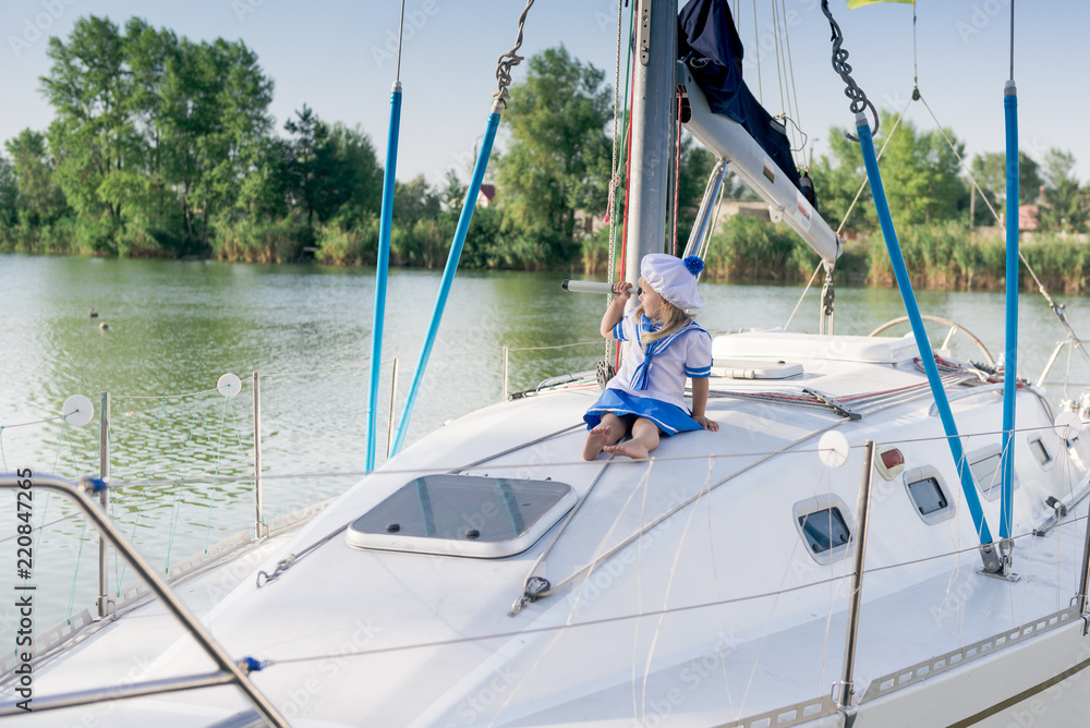 Obraz premium Funny little baby captain on board of sailing yacht watching offshore sea on summer cruise. Travel adventure, yachting with child on family vacation. Kid clothing in sailor style, nautical fashion.