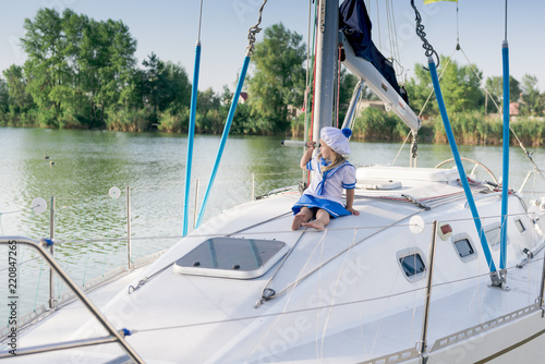 Funny little baby captain on board of sailing yacht watching offshore sea on summer cruise. Travel adventure, yachting with child on family vacation. Kid clothing in sailor style, nautical fashion. photo