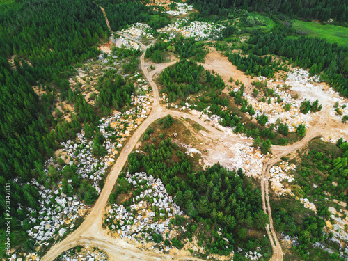 Aerial view of opencast mining quarry with of machinery at work, white quarry stones scattering on the working area in the forest. mine environment, industry background, antropogenic landscape, Russia photo